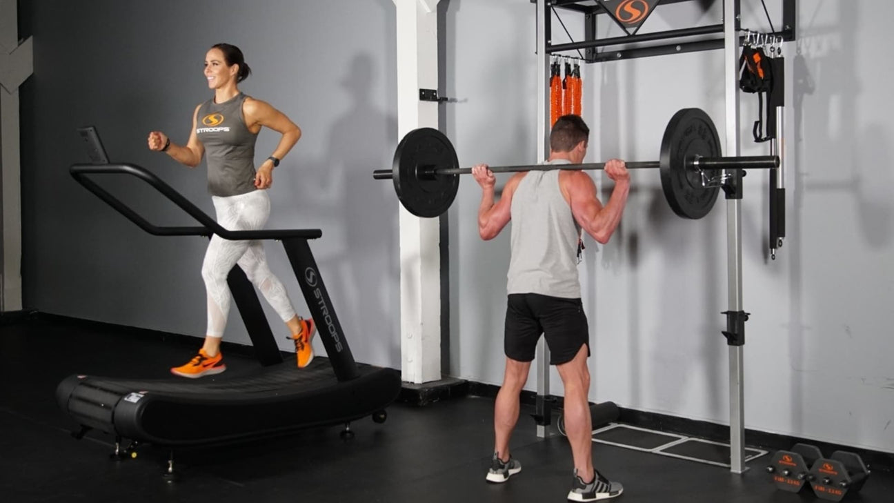 woman using stroops curved treadmill while man squats using stroops wall mounted power rack