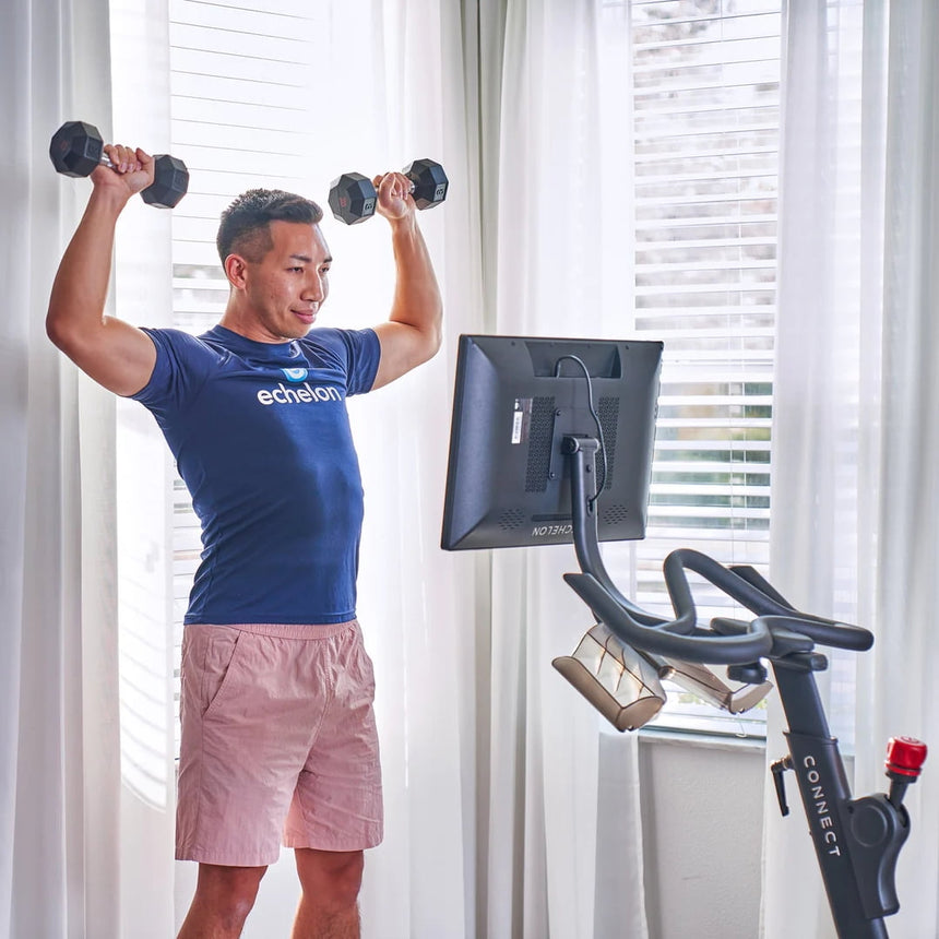 Man using Echelon EX-5s Smart Connect Bike in living room  and lifting weights