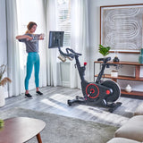 Woman using Echelon EX-5s Smart Connect Bike in living room  and weights
